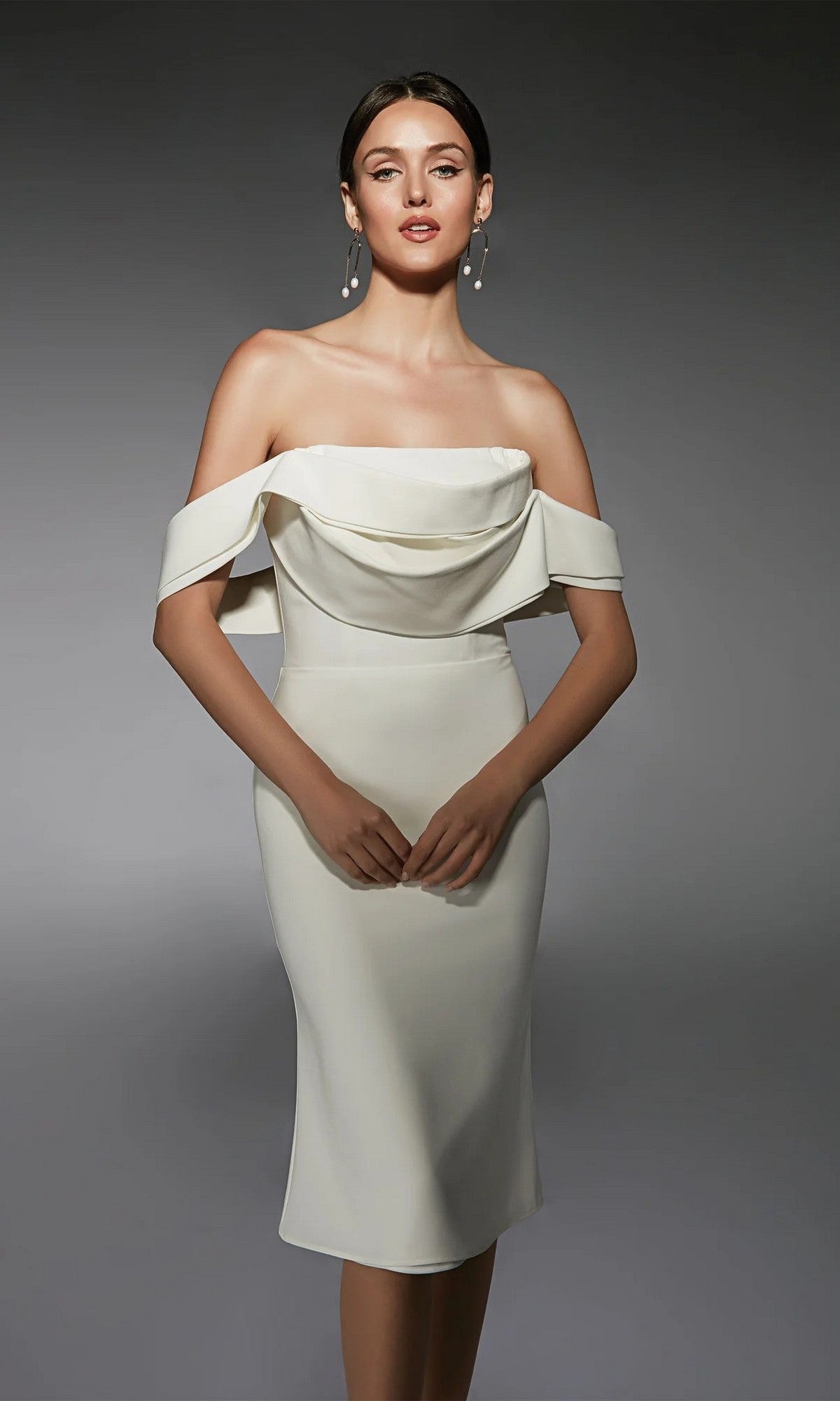Woman wearing the Alyce 70055 knee-length semi-formal dress in ivory, featuring off-the-shoulder draped sleeves, styled as a chic sheath, standing against a plain gray background.
